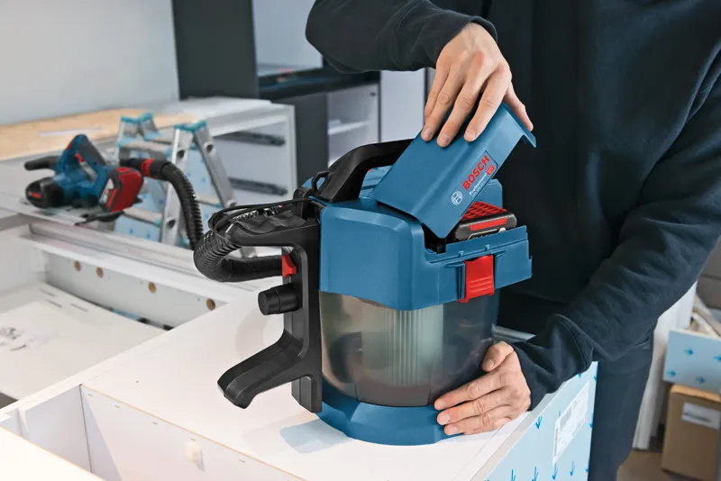 Một người lắp pin vào máy hút bụi không dây trên bàn làm việc.