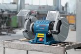 Máy mài hai bánh xe đặt trên bàn làm việc bằng kim loại trong xưởng công nghiệp.