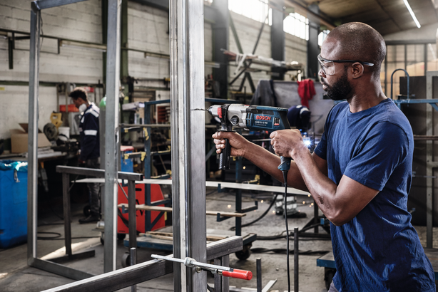 Object #200255101: Bosch_HSS_Point_Location22647 Người mặc đồ bảo hộ đang khoan vào khung kim loại trong một xưởng công nghiệp.