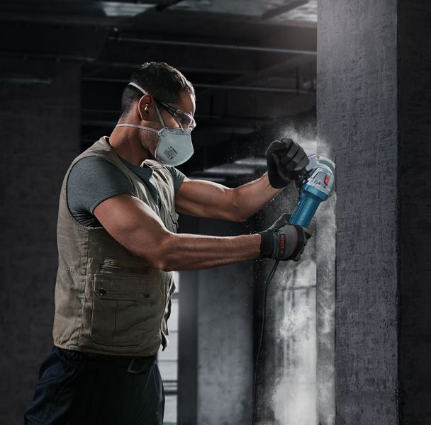 Một người mặc đồ bảo hộ đang mài bức tường bê tông bằng máy mài góc.