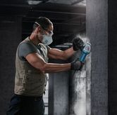 Một người mặc đồ bảo hộ đang mài bức tường bê tông bằng máy mài góc.