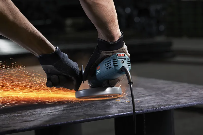 GWS 900-100 S Một người mặc đồ bảo hộ sẽ mài kim loại, tạo ra tia lửa sáng.