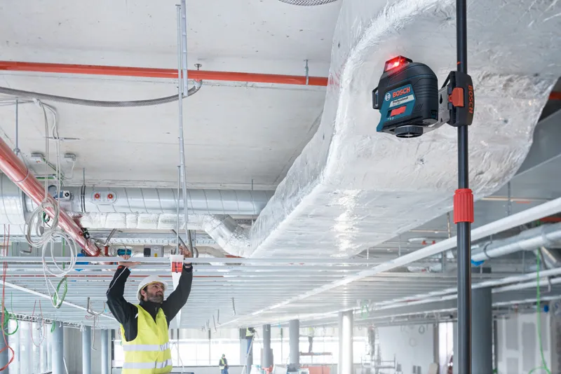 Một người mặc thiết bị an toàn đang căn chỉnh khung trần nhà bằng dụng cụ cân bằng laser.