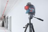 Máy cân bằng laser chiếu những đường màu đỏ lên trần nhà khi một người đang làm việc trên thang.