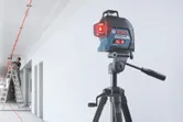 Máy cân bằng laser chiếu những đường màu đỏ lên trần nhà khi một người đang làm việc trên thang.