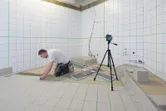 Người đang lắp gạch ốp lát trong phòng tắm, sử dụng máy cân bằng laser trên chân máy.