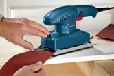 Một người dán giấy nhám vào máy chà nhám quỹ đạo đặt trên bề mặt gỗ.