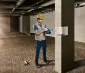 Một người đàn ông mặc đồ bảo hộ đang khoan vào một trụ bê tông tại công trường xây dựng.