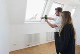 Một người đang hướng dẫn người khác sử dụng camera nhiệt gần cửa sổ trong một căn phòng sáng.