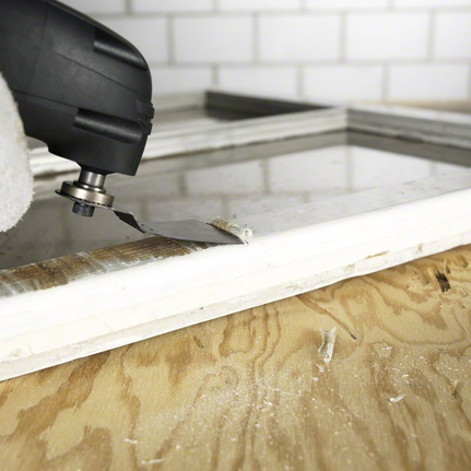 Một người đàn ông mặc đồ bảo hộ đang sử dụng dụng cụ đa năng để loại bỏ vật liệu khỏi khung cửa sổ.