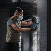 Một người mặc đồ bảo hộ đang sử dụng máy mài góc trên bức tường bê tông.