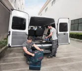 Hai công nhân gần một chiếc xe tải mui trần đang sắp xếp dụng cụ và sử dụng máy hút bụi không dây.