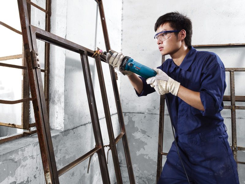 Người đeo thiết bị an toàn sử dụng máy mài thẳng trên khung cửa sổ kim loại.