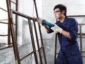 Một người mặc đồ bảo hộ đang mài khung kim loại bằng máy mài thẳng.