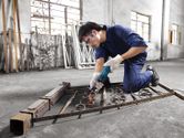 Một người mặc đồ bảo hộ đang mài kim loại cuộn bên trong xưởng.