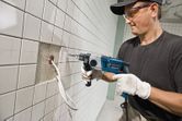 Một người mặc đồ bảo hộ đang khoan vào bức tường gạch phía trên các dây cáp lộ ra.