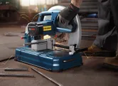 Một người mặc đồ bảo hộ đang cắt thanh thép bằng máy cưa cố định, tia lửa bắn ra.