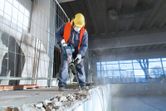 Một người mặc thiết bị an toàn đang sử dụng búa phá dỡ để phá bê tông trong nhà.