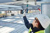 Một người mặc thiết bị an toàn sử dụng cờ lê tác động không dây trên một thanh kim loại.