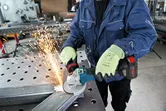 Một người mặc đồ bảo hộ sẽ mài kim loại bằng máy mài góc, tạo ra tia lửa.