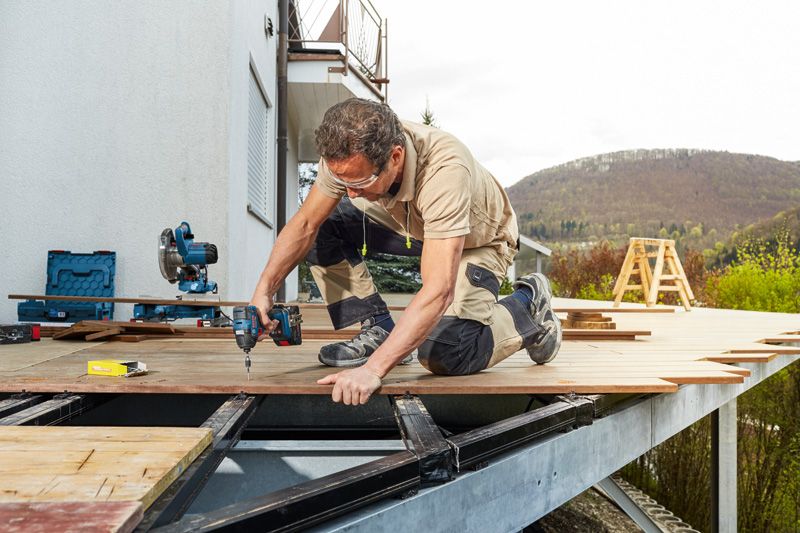 Một người mặc thiết bị an toàn sử dụng máy vặn vít không dây để cố định ván sàn.