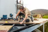 Một người mặc thiết bị an toàn sử dụng máy vặn vít không dây để cố định ván sàn.