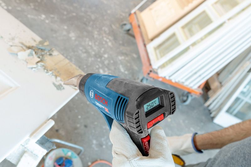 GHG 20-63 Một người mặc đồ bảo hộ sử dụng súng nhiệt để loại bỏ sơn trên cửa.