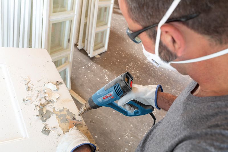 GHG 20-63 Người mặc thiết bị an toàn sử dụng súng nhiệt để cạo lớp sơn trên cửa.
