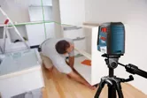 Một người đang lắp tủ trong bếp bằng cách sử dụng máy cân bằng laser trên giá ba chân.