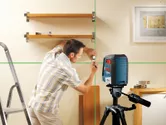 Một người đang đánh dấu tường để lắp kệ bằng công cụ cân bằng laser màu xanh lá cây.