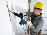 Một người mặc thiết bị an toàn đang sử dụng búa phá dỡ để phá tường.