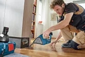 Một người mặc đồ bảo hộ sử dụng máy hút bụi không dây để hút sạch vụn gỗ.