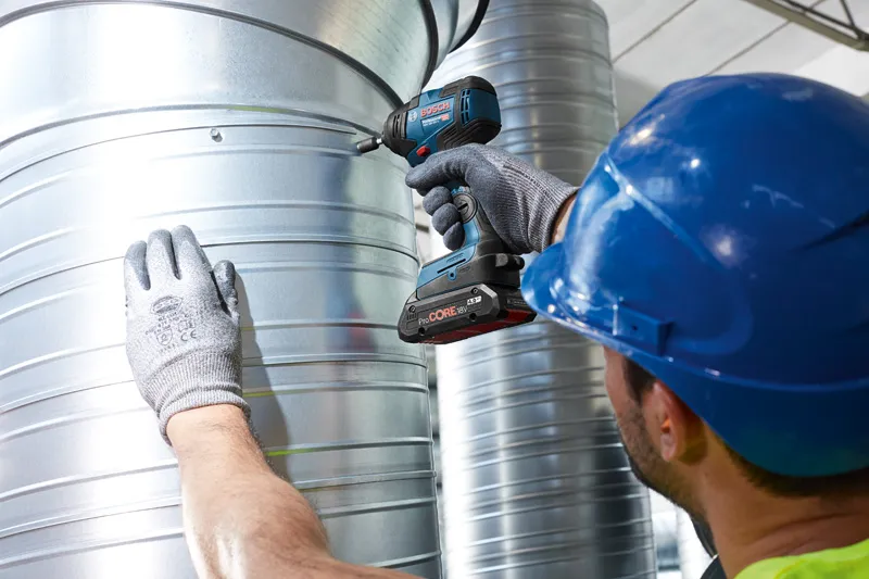 Một người mặc thiết bị an toàn sử dụng máy siết bu lông không dây vào ống dẫn khí bằng kim loại.