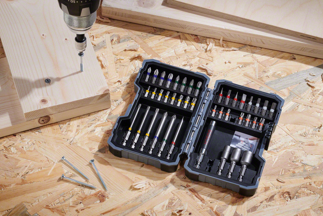 Máy khoan được đặt trên bề mặt ván ép, bên cạnh các ốc vít và tấm ván gỗ.