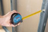 Một người sử dụng thước dây để kiểm tra khoảng cách giữa vách thạch cao và khung kim loại.