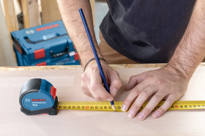 Người đánh dấu số đo trên gỗ bằng bút chì và thước dây.