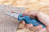 Một người đang cầm một con dao rọc giấy, chuẩn bị cắt một miếng thảm.