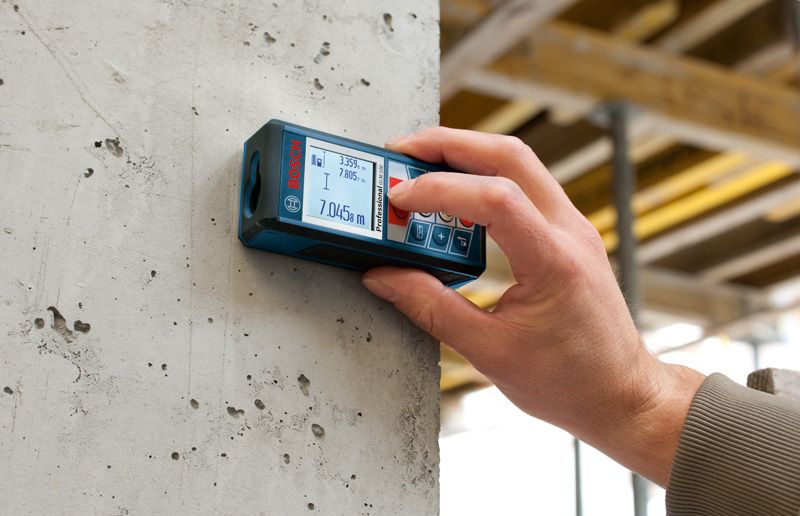 Một người đang sử dụng máy đo laser trên bức tường bê tông tại một công trường xây dựng.