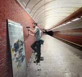 Một người sử dụng máy khoan không dây để gắn khung vào tường gạch ở ga tàu điện ngầm.