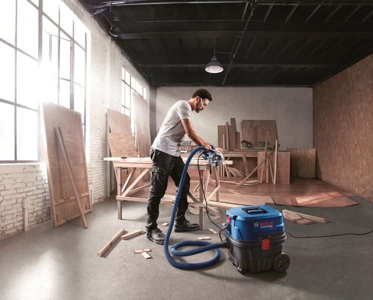 Một người mặc đồ bảo hộ đang sử dụng máy hút bụi trong xưởng chế biến gỗ.