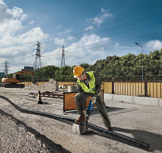 GSA 120 Một người mặc đồ bảo hộ đang sử dụng máy cưa lọng để cắt ống tại công trường xây dựng.