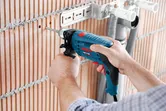 Một người đang khoan vào bức tường gạch gần các ống kim loại và giá đỡ.