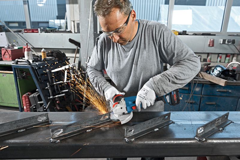 Một người đàn ông mặc đồ bảo hộ đang dùng máy mài góc không dây để mài kim loại, tạo ra tia lửa.