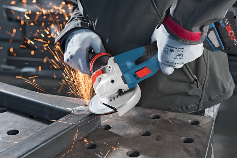 GWX 18V-15 C Một người mặc đồ bảo hộ đang mài một thanh kim loại bằng máy mài góc không dây.