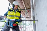 Một người mặc đồ bảo hộ đang khoan bê tông bằng búa quay không dây.