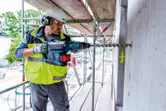Một người mặc đồ bảo hộ đang khoan vào bức tường bê tông tại một công trường xây dựng.