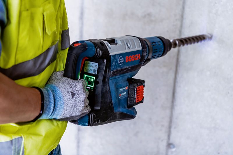 GBH 18V-45 C Một người mặc đồ bảo hộ đang khoan vào bê tông bằng một chiếc búa quay lớn.