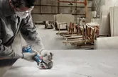 Một người mặc đồ bảo hộ đang cắt tấm đá bằng máy mài góc không dây trong xưởng.