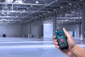 Một người sử dụng máy đo laser trong một nhà kho công nghiệp rộng lớn và trống rỗng.