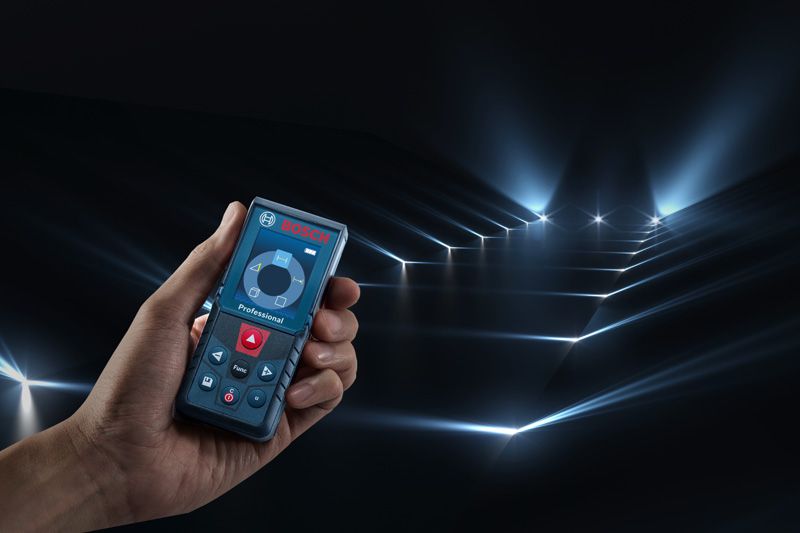 Người cầm thước đo laser chiếu nhiều chùm tia đo qua một căn phòng tối.